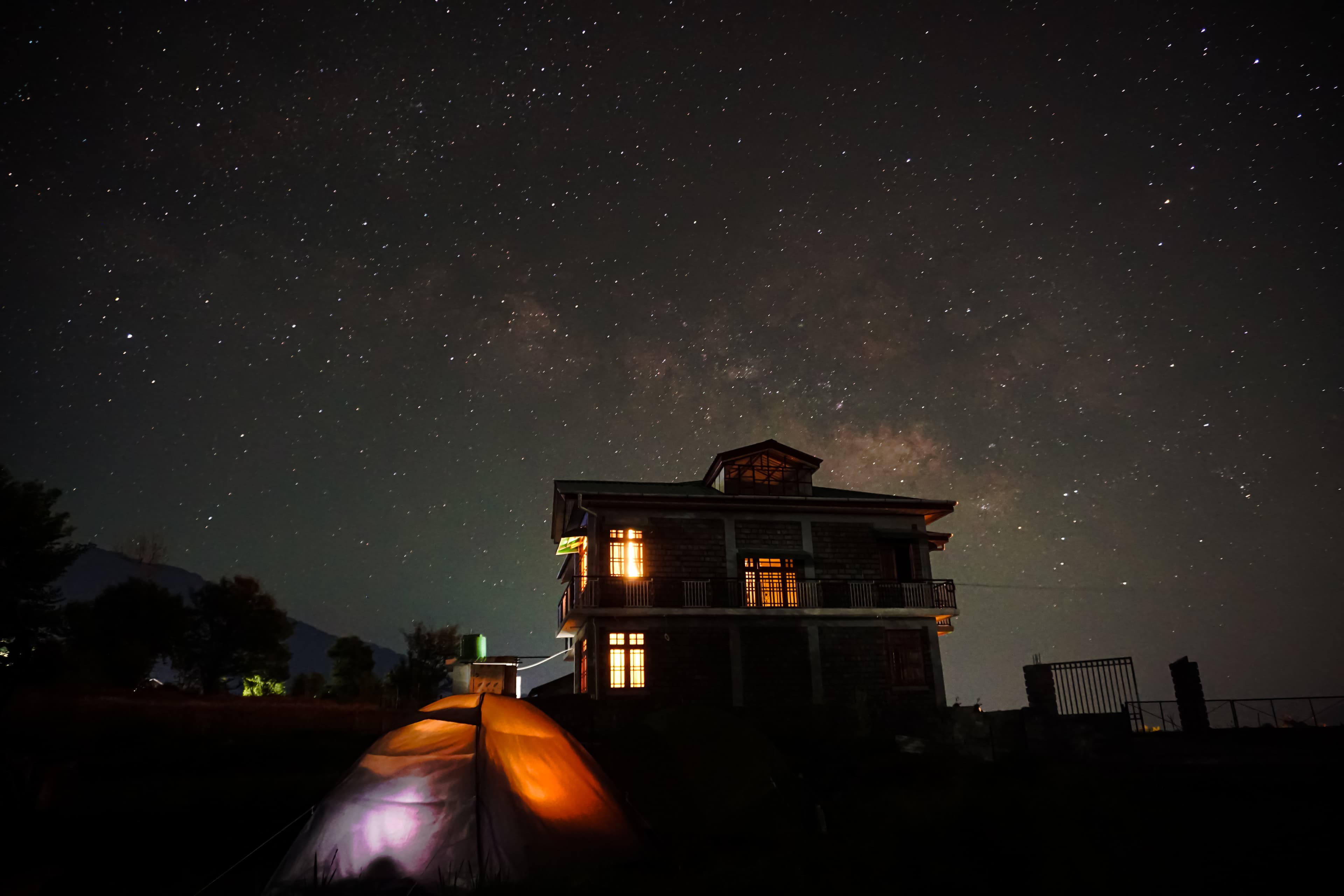 Starry night sky with Milky Way over illuminated building and tent
